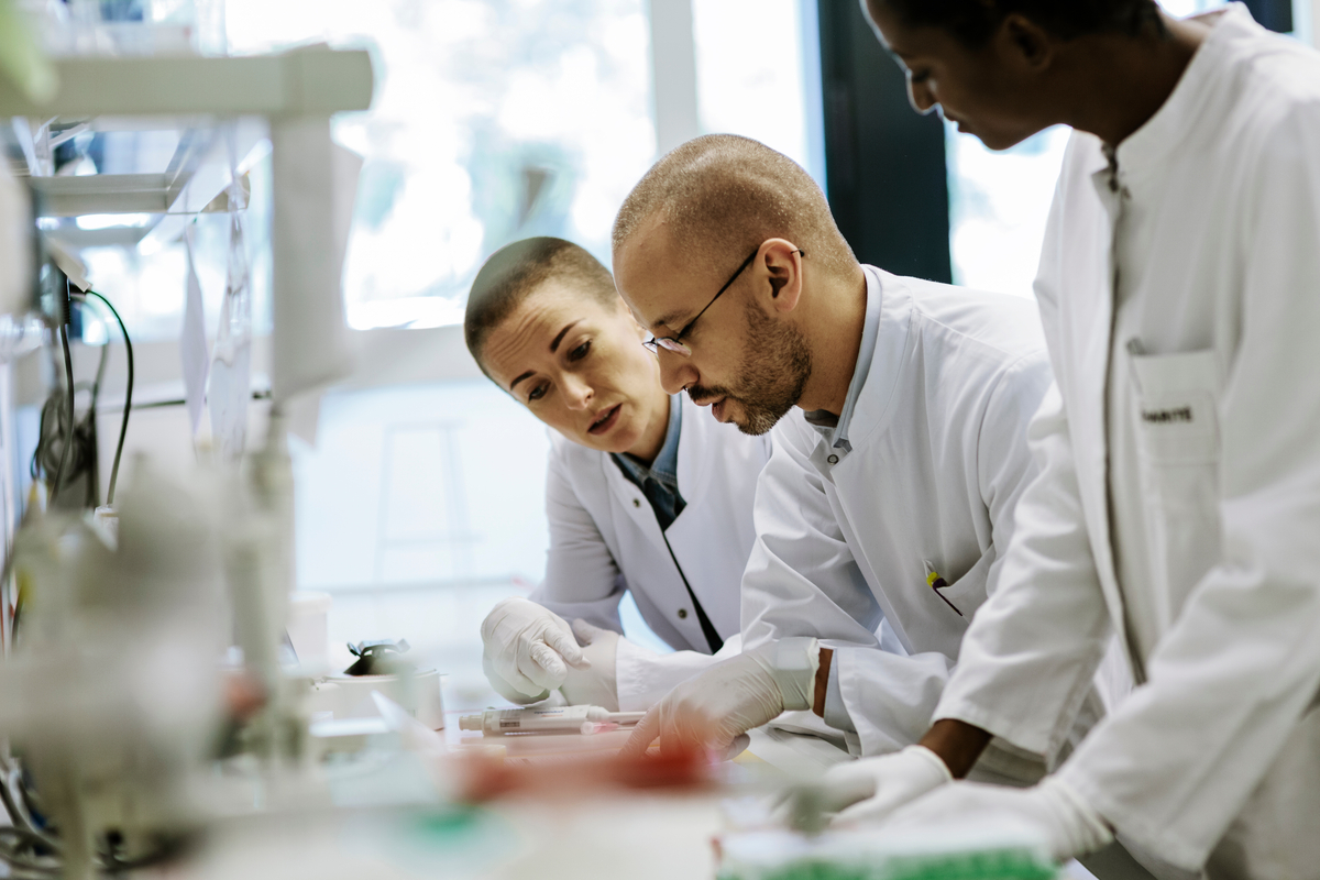 Three scientists working in a laboratory. They are bending over a table looking at data and a paper.